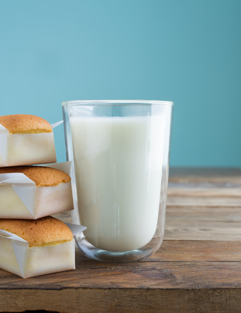 蓝色背景的木桌上放着杯形蛋糕和牛奶。副本的空间。垂直的照片。手工制作的玛德琳蛋糕。图片下载