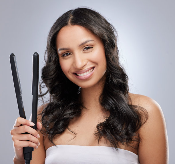 一名年轻漂亮的女子手持直发器，站在灰色的背景下图片下载