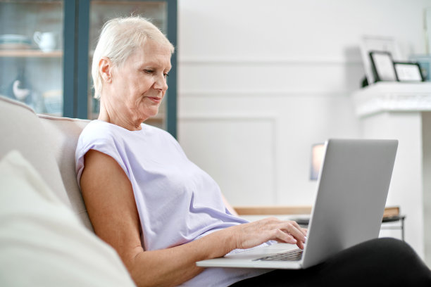 一位老妇人坐在一台打开的笔记本电脑前做瑜伽图片下载