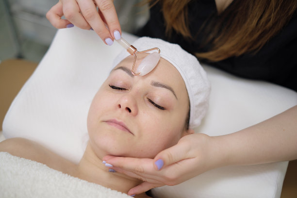 平静的病人正在进行面部美容按摩。美容院用刮痧石做美容的女人图片下载