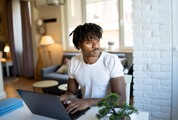 一个男人一边看着窗外，一边在笔记本电脑上工作图片下载