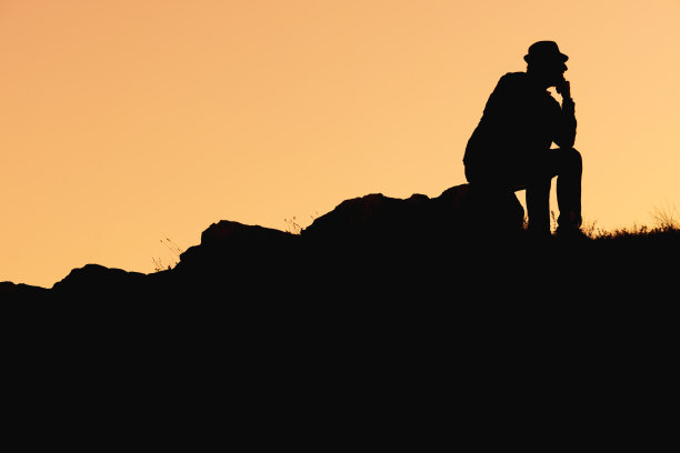 一个戴帽子的人的剪影，以思考者的姿势坐在上升线上的石头上图片下载