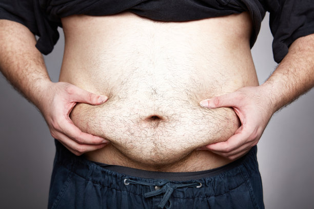 一名男子挤压过多的腹部脂肪和灰色背景上的妊娠纹。图片下载