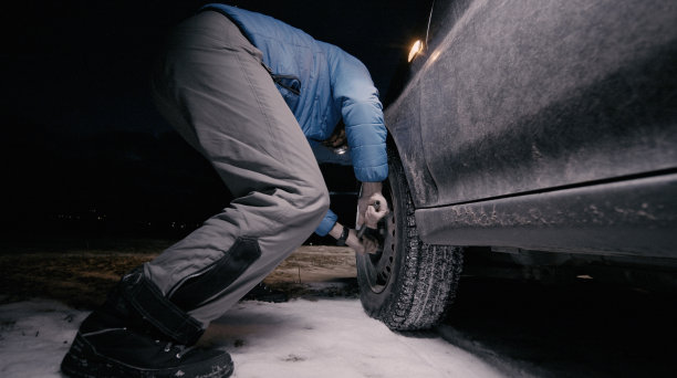 男人在冬天的夜晚给汽车换轮胎。图片下载