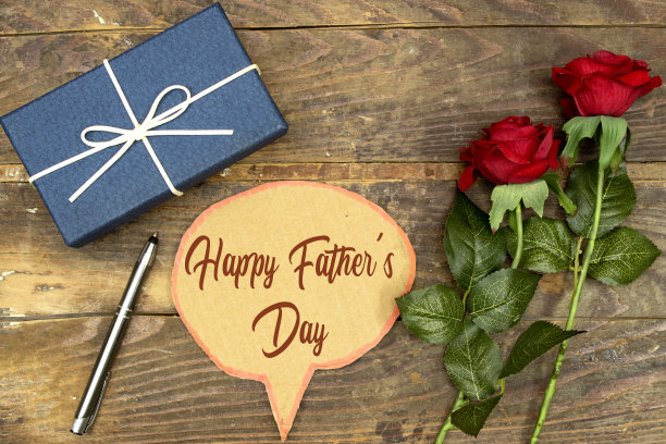 红玫瑰花与快乐的父亲节聊天气泡纸盒卡片和蓝色的礼盒在木桌子上图片下载