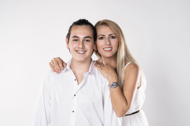 金发长发的母亲微笑着，在白色的背景下看着镜头的十几岁的儿子。图片下载