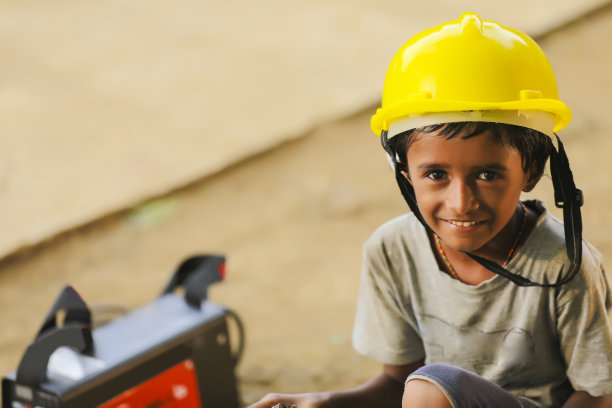 可爱的亚裔印度小孩戴着黄色的建筑头盔或安全帽。图片下载