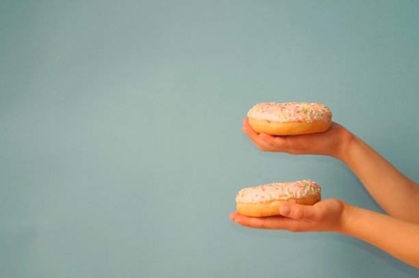 孩子手里拿着两个点缀着五颜六色的甜甜圈，背景是灰蓝色的。关注最上面的甜甜圈。手移到边缘，有一个地方可以放你的笔记，复制空间图片下载