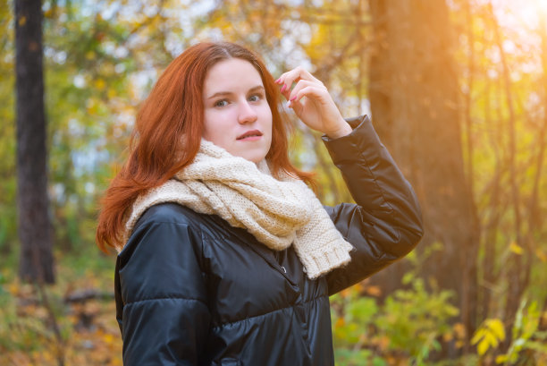 照片中，一个红头发的女孩穿着夹克和围巾，在秋天的自然和明亮的太阳的背景下，微笑着直发图片下载