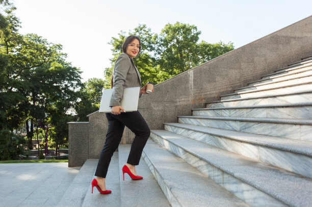 女商人拿着笔记本电脑和一杯咖啡边走边爬上楼梯图片下载