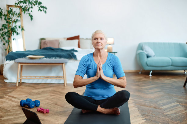 一位老妇人坐在一台打开的笔记本电脑前做瑜伽图片下载