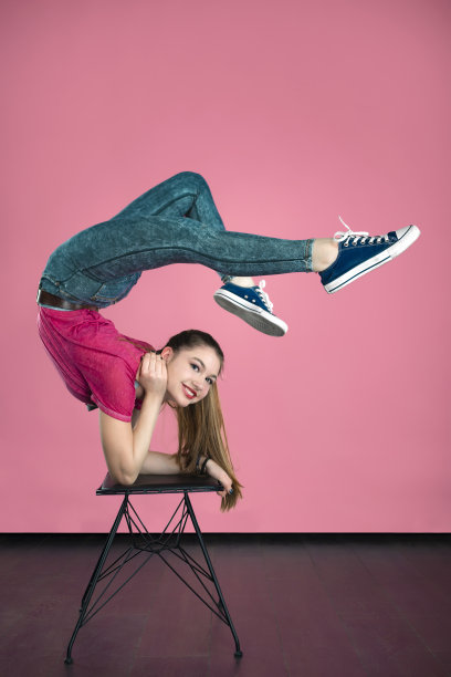 一个十几岁的女孩在一个以粉红色为背景的工作室里做着运动。图片下载