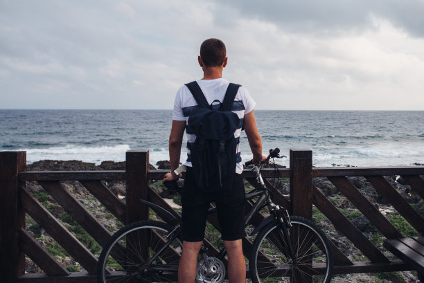 骑着自行车的年轻人站在海边看海看天。图片下载