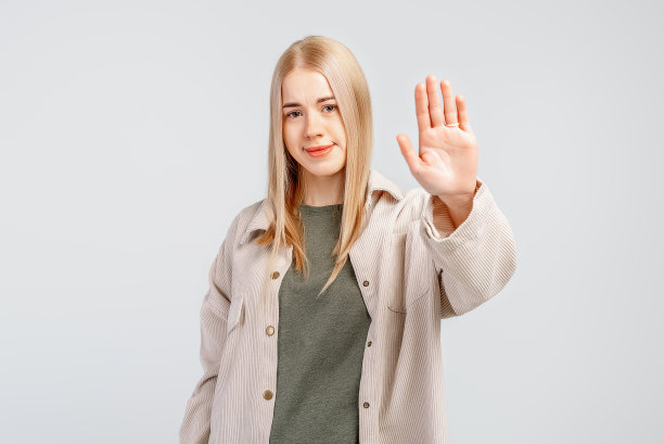 一个严肃的年轻金发女人的肖像，伸出的手显示停止的手势，拒绝允许，灰色的背景图片下载