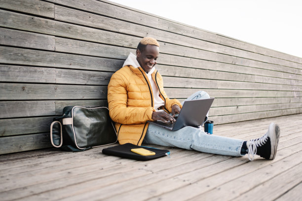 年轻时尚的非裔美国人坐在户外工作的笔记本电脑微笑。学生、自由职业者、在线创业者图片下载