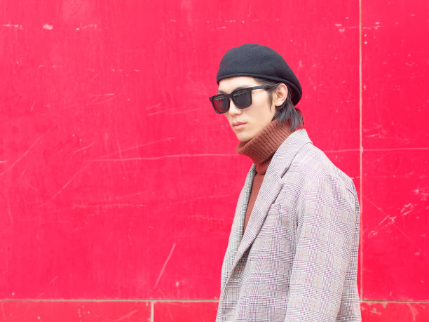 英俊的中国年轻人的肖像，穿着休闲西装和太阳镜，在红色的墙壁背景下摆姿势。边走边看摄像头，看起来很自信，侧视。图片下载