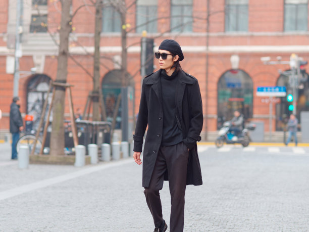 帅气的中国年轻男子身穿黑色大衣，毛衣和裤子，戴着太阳镜走在上海的街道上，正面，男性时尚，酷的亚洲年轻人的生活方式的肖像。图片下载