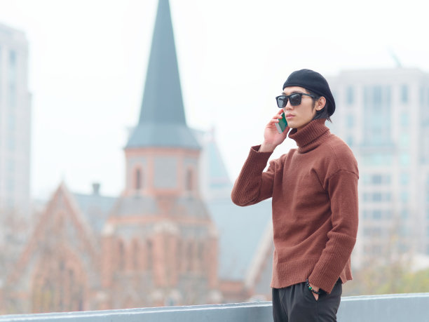 英俊的中国年轻男子的肖像太阳镜站和说话在手机与手在口袋里与上海城市地标背景，男性时尚，酷的亚洲年轻男子的生活方式。图片下载