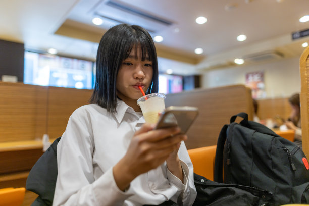 十几岁的女孩在咖啡厅喝果汁，用智能手机图片下载