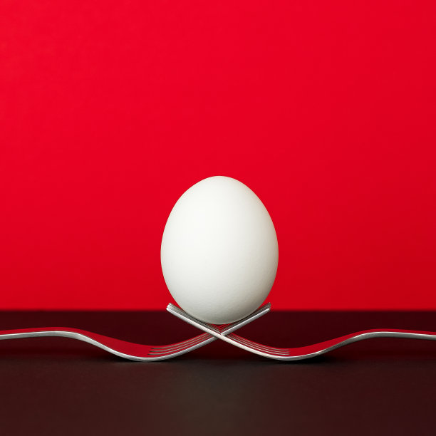 鸡蛋平衡在两个金属叉子，红色和黑色的背景。图片下载