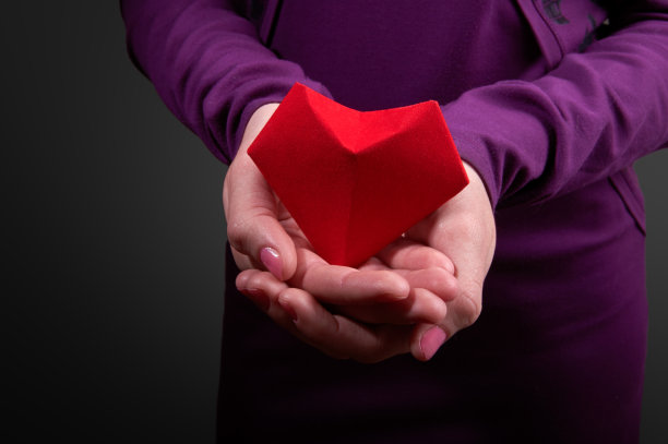 象征女性手掌中的心。红色的纸心在女人的手上，黑色的背景。特写镜头图片下载