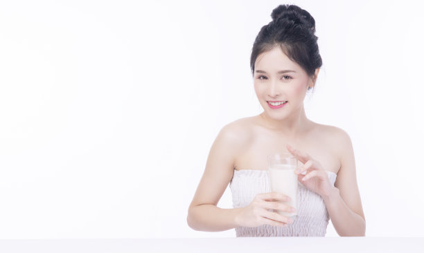 迷人可爱苗条的亚洲妇女与玻璃新鲜牛奶饮料为良好的健康皮肤，而坐在白色的桌子上孤立的白色背景。保健钙质食品，健身理念。图片下载