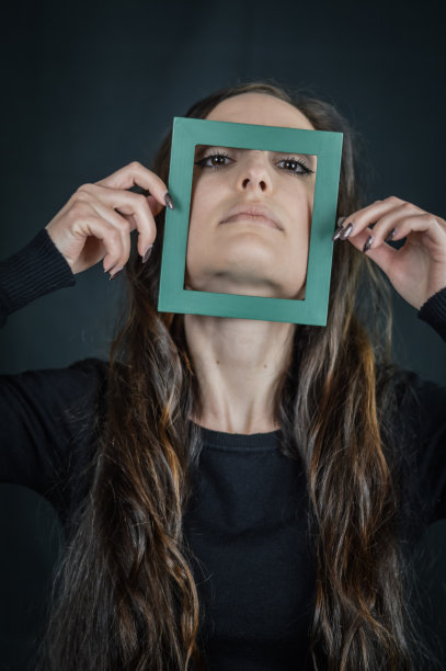 相框的美丽-一个美丽的黑发女人的肖像，在她的脸前拿着一个小的相框-独特和多样性的概念图片下载