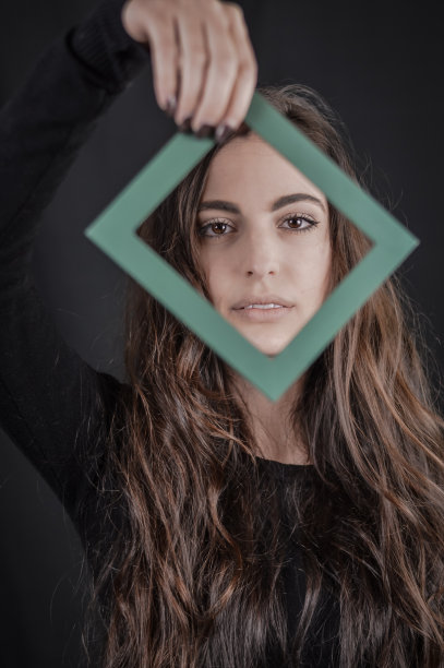 相框的美丽-一个美丽的黑发女人的肖像，在她的脸前拿着一个小的相框-独特和多样性的概念图片下载