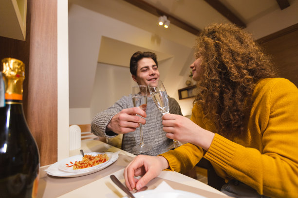 美丽的年轻夫妇在家里吃浪漫的晚餐时，用酒杯里的香槟欢呼/干杯图片下载
