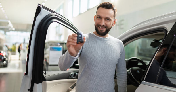 经销商展厅里，一辆新车的车主手里拿着一把钥匙，开心地看着车外图片下载