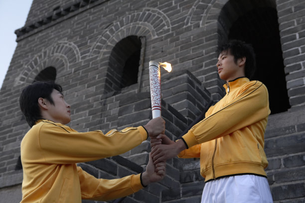 两位身穿运动服的年轻人站在长城烽火台前，举着一支火炬图片下载