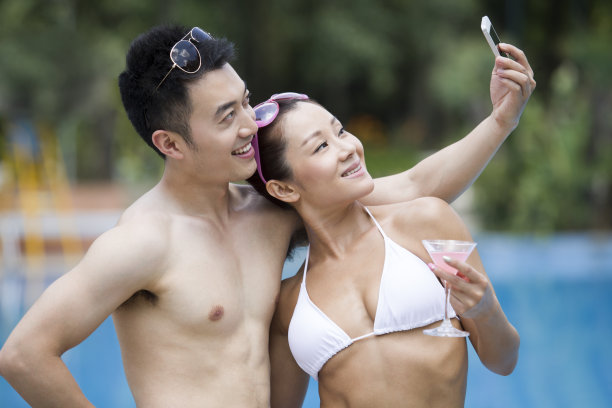 年轻情侣在泳池边拍照图片下载