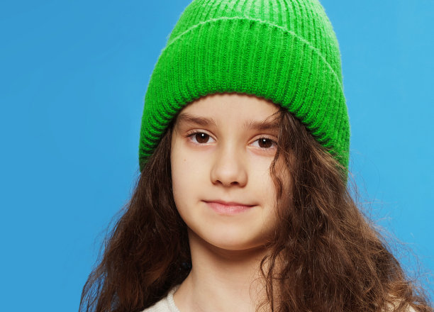 一个可爱的小女孩的肖像，绿色的帽子和波浪的头发，孤立在蓝色的背景图片下载