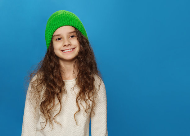 肖像迷人，开朗，带着绿帽子和波浪头发的小女孩，现代潮流，孤立在蓝色的背景上图片下载