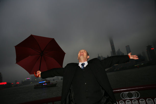 阴雨天外滩黄浦江边一位外国商务人士拿伞张开双臂图片下载