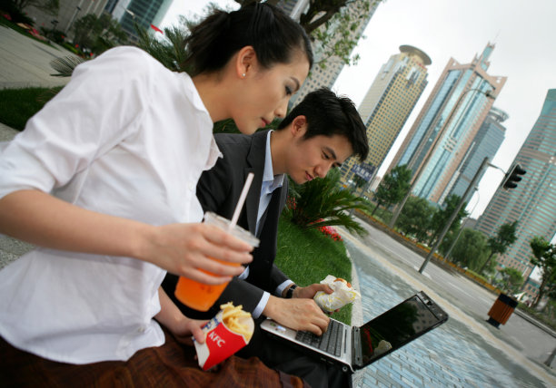 上海浦东写字楼旁两位商务人士使用笔记本电脑时吃洋快餐图片下载