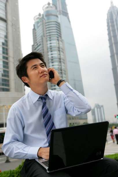 上海浦东金茂大厦前一位男商务人士使用笔记本电脑时打手机图片下载