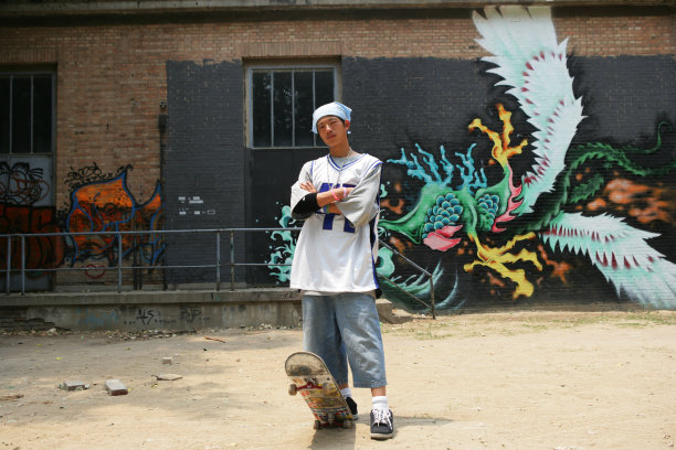 滑板男青年站在798艺术区内的涂鸦画前图片下载