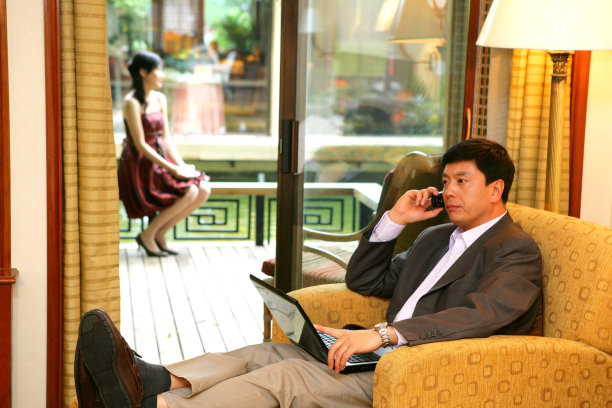 商务人士在酒店房间里边打电话边使用笔记本电脑图片下载