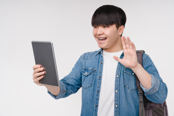 一名年轻的韩国亚裔男生在大学学院用数码平板电脑进行在线学习、视频通话、远程在线学习图片下载