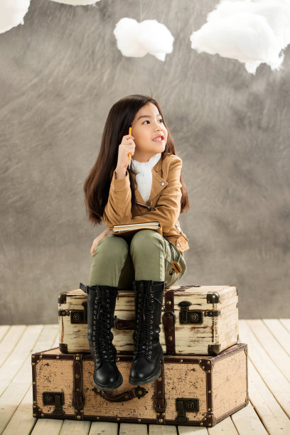 小女孩拿着笔记本坐在行李箱上思考图片下载