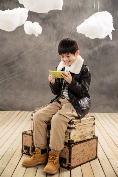 小男孩坐在复古行李箱上玩游戏机图片下载
