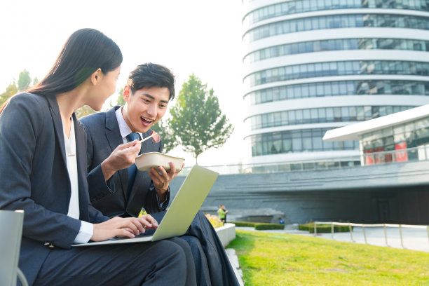 青年商务人士坐着户外边吃饭边工作图片下载