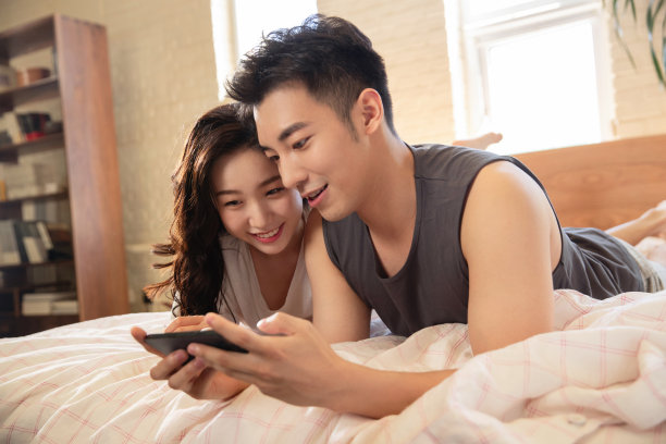 青年情侣趴在床上玩手机图片下载