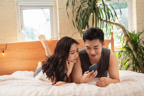 青年情侣趴在床上玩手机图片下载