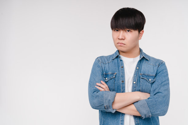 冒犯伤心愤怒的年轻亚洲韩国男子学生男孩吹他的嘴唇与双臂交叉孤立在白色背景图片下载