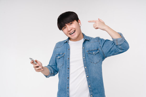 跳舞活跃的亚洲韩国青年男子男孩学生听着音乐，用手机指着显示耳机，选择原声带，播放列表，收音机孤立在白色背景上图片下载