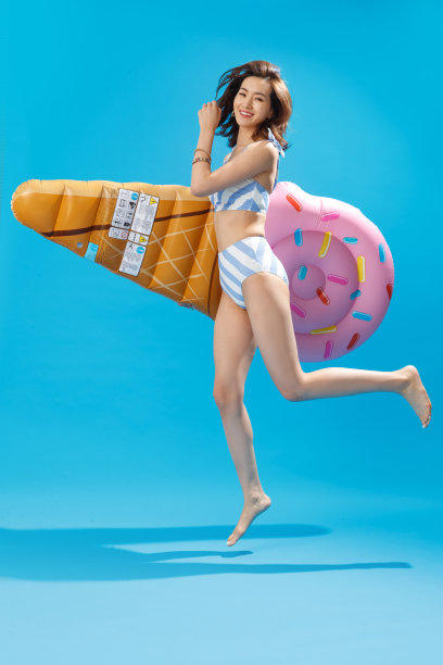 抱着冰淇淋形状的浮排跳跃的泳装美女图片下载
