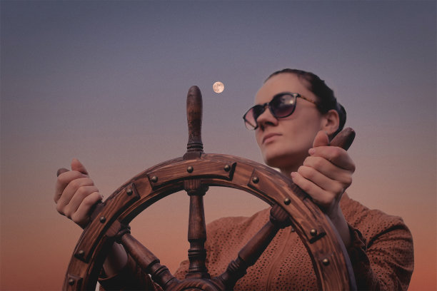 女孩控制着游艇，双手握着方向盘，手轮在天空的背景上图片下载