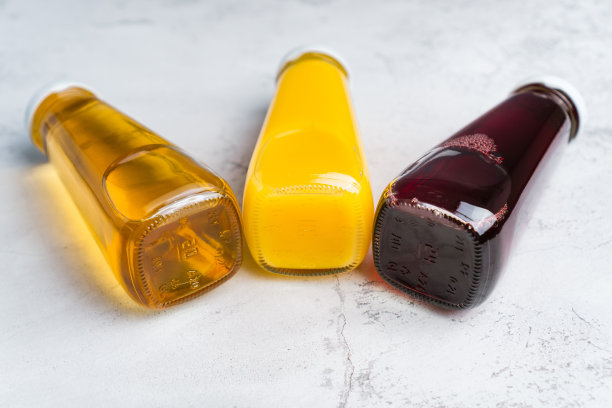 黄色和红色液体健康饮料在灰色背景上的瓶子。橙苹果樱桃汁图片下载